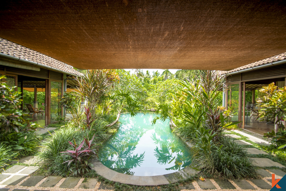 Lush garden and pool view from under the shade of an Ubud villa's overhanging roof, showcasing tropical landscaping and the integration of natural elements in Balinese architecture.